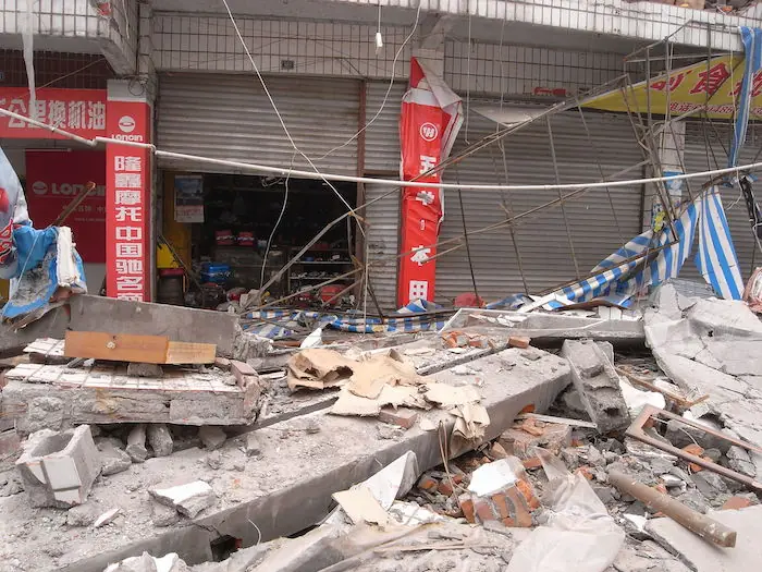The image shows The outside of a warehouse in disarray following the earthquake.